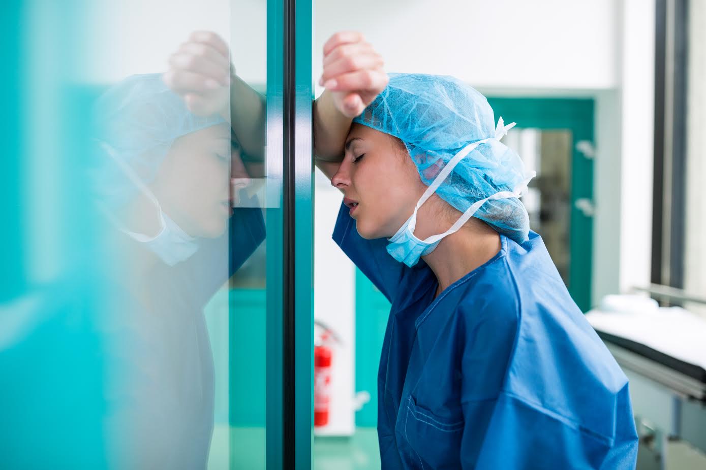 Sad surgeon leaning against the glass door in hospital